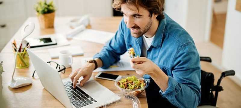 Young man in wheelchair eating while on laptop.