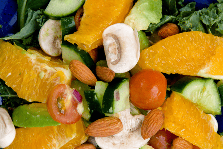 Various cut up vegetables and oranges on a blue plate