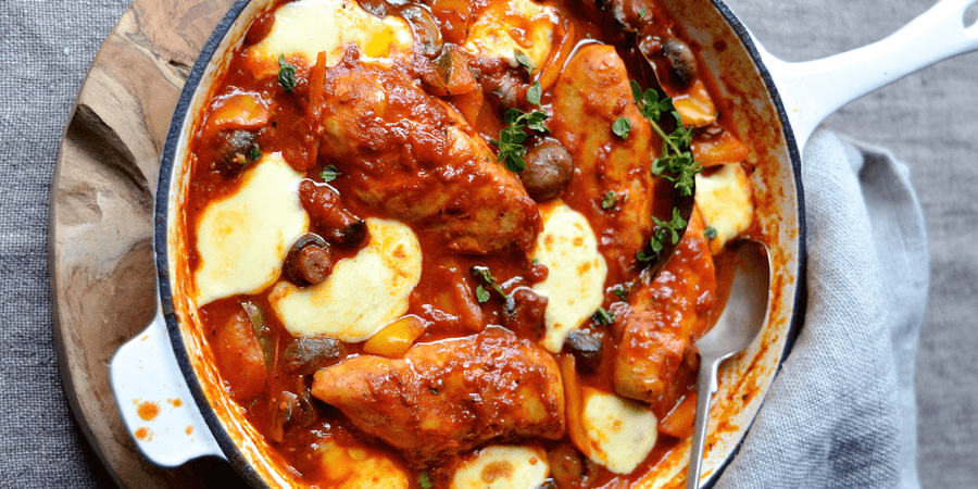 Mediterranean chicken served in a saucepan on a wooden board.