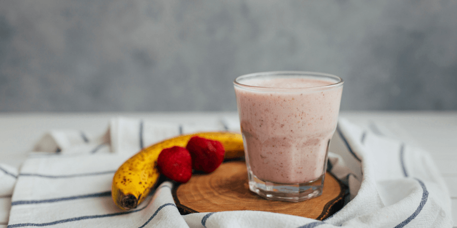 Strawberry smoothie in a glass next to a banana and some strawberries